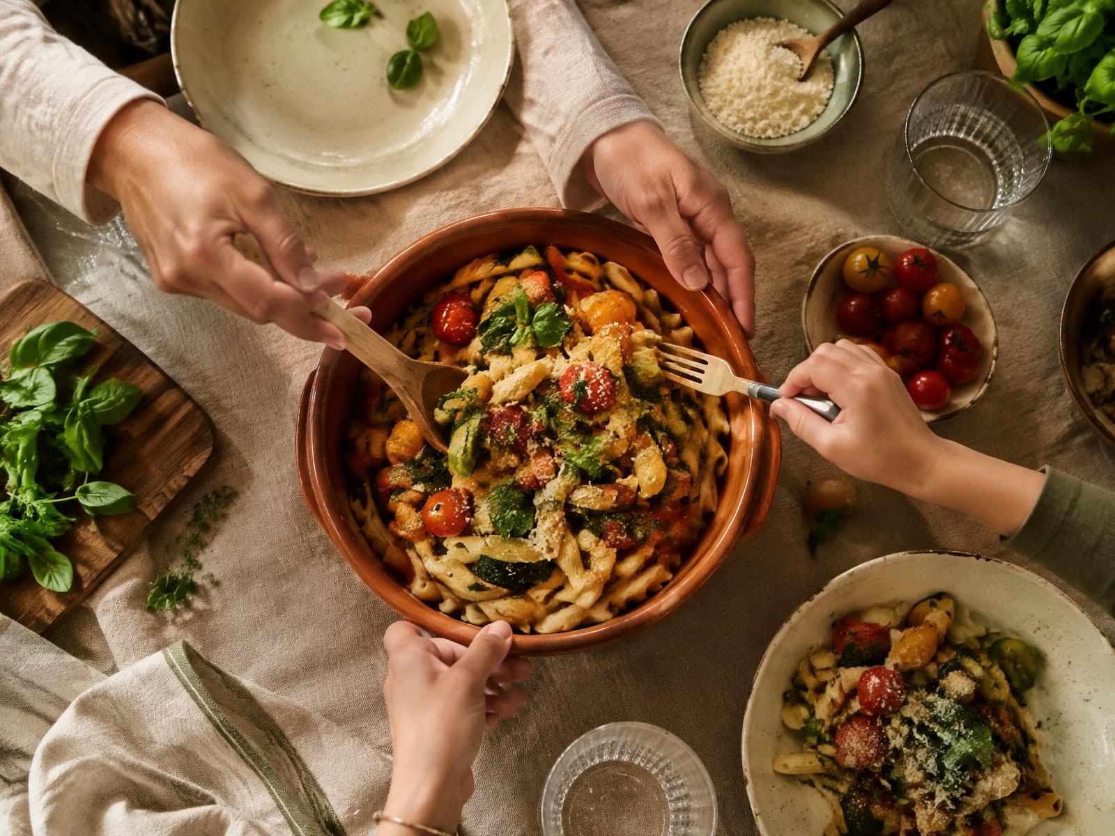 Een gezin schept samen pasta met groente uit een terracotta schaal